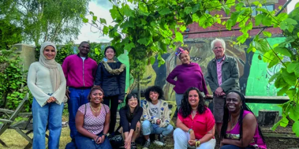 A group of people in front of some plants, together for a photo. Some are crouched, some are stood up.