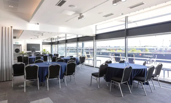 Conference style room with tables in front of a screen. 
