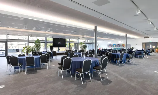 Conference style room with tables in front of a screen. 
