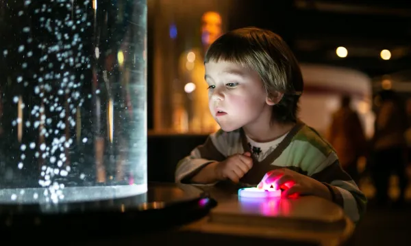 A young child playing with an exhibit and watching bubbles blow up in front of their face