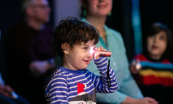 A small child is holding a torch up to it's eye, in a studio space.