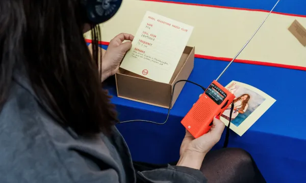 A person is sat at a desk holding an old radio and a piece of paper.