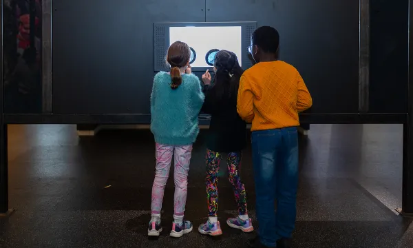 Three children look at an interactive exhibit through large magnifying glasses.