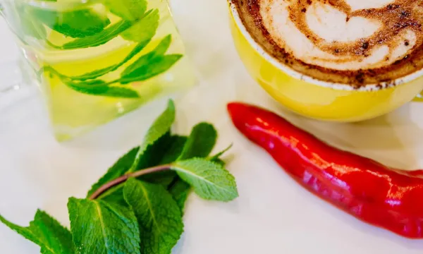 A jug of mint tea and a spicy hot chocolate in a festive activity in We The Curious. There are mint leaves and a red chilly on the table by the cups.