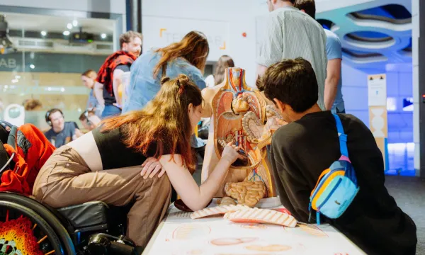 Two people are sat Infront of an anatomical model of a body placing objects into it.