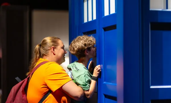 An adult is lifting up a child to peer into the TARDIS in a science centre.