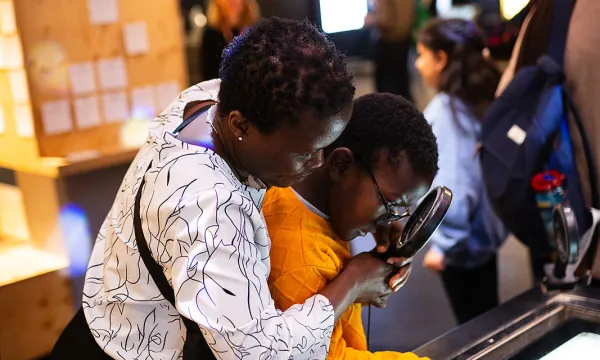 A person holding a magnifying glass helping a child explore and exhibit together in an interactive science centre. 