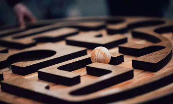 A wooden panel with a maze carved into it with a wooden ball resting on top of it.