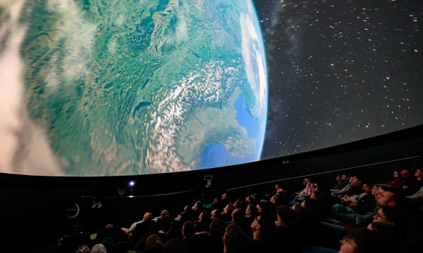 Image shows view of audience in the planetarium. On the screen is an image of Earth from orbit.