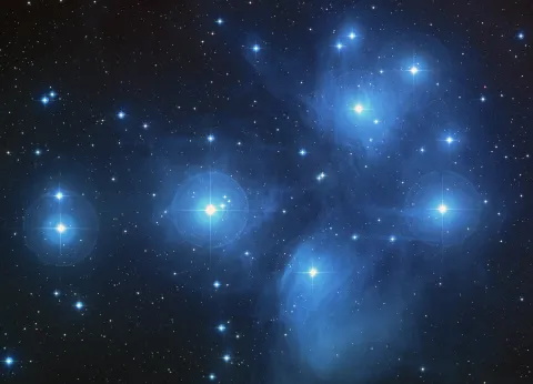 A dark blue night sky with lots of white stars dotted across it surrounded by light blue clouds.