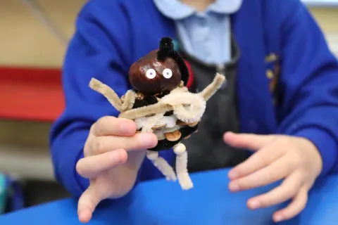 A little humanoid model made from a conker and pipecleaners, being held by a child 