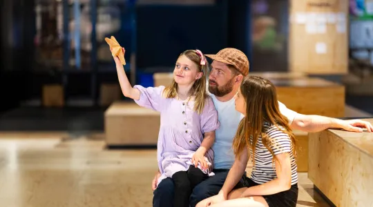 A man wearing a baseball cap and two children holding up a star shell in We The Curious