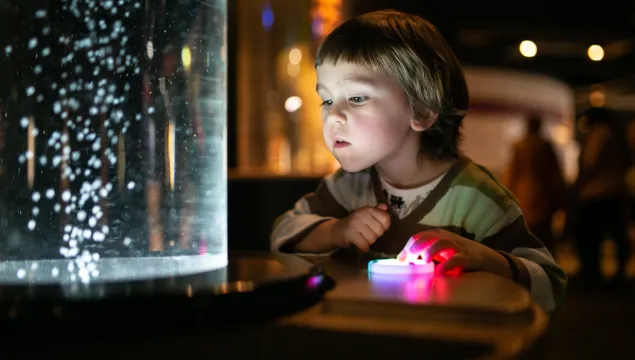 A young child playing with an exhibit and watching bubbles blow up in front of their face