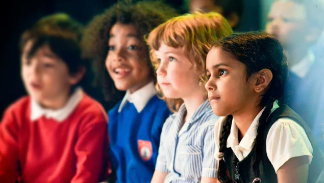 A group of 4 primary school children - looking off camera to the left, some concentrating, some smiling. 