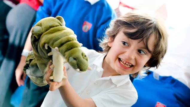 A child smiling and playing with a crocodile puppet