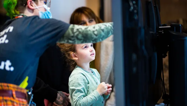 A young child is looking up at a digital screen, which a We The Curious member staff is pointing to