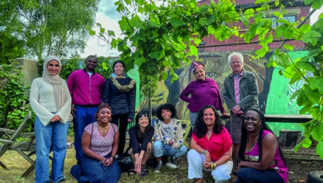 A group of people in front of some plants, together for a photo. Some are crouched, some are stood up.
