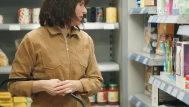 A person in a supermarket, carrying a shopping basket and looking at items.