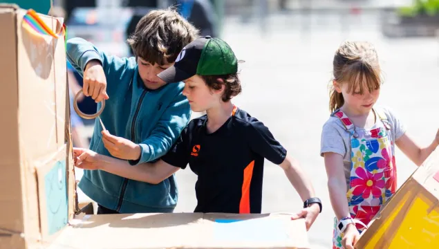 Three children building with cardboard and Sellotape on Millennium Square