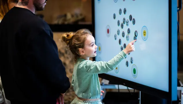 A child in a light green outfit pointing at a digital screen with lots of circular shapes