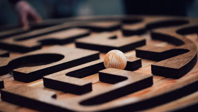 A wooden panel with a maze carved into it with a wooden ball resting on top of it.