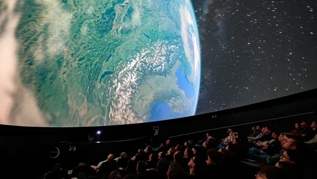Image shows view of audience in the planetarium. On the screen is an image of Earth from orbit.