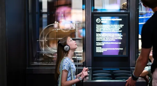 A child wearing headphones listens to stories in the Time exhibit at We The Curious. They are looking up at the exhibit.