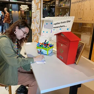 Dr Romana Burgess writes a postcard to a visitor while visiting the Open City Lab.