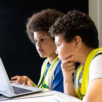 Two primary school aged children sat at a table with a laptop, working together on a project or game. Credit Freia Turland
