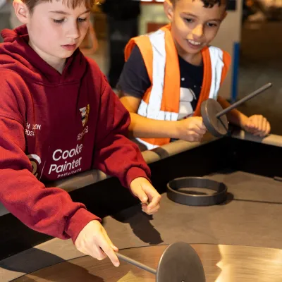 Two primary school aged children playing with a spinning metal disk exhibit inside We The Curious. Credit Freia Turland