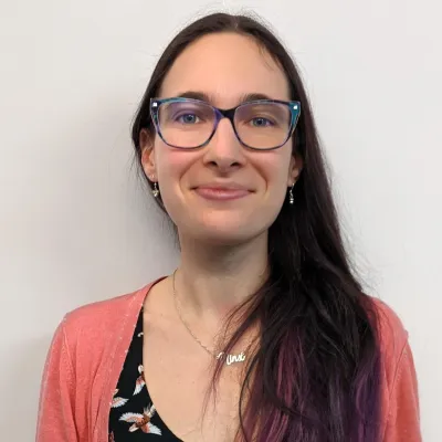 Headshot of a person with long dark hair and glasses 