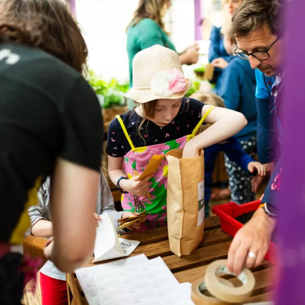 A child in a light sunhat and bright overalls putting seeds in a paper bag