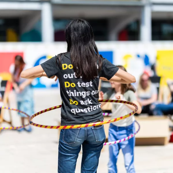 A We The Curious staff member facing away from the camera, hulahooping. Their t-shirt reads 'Do test things out, Do ask questions' 