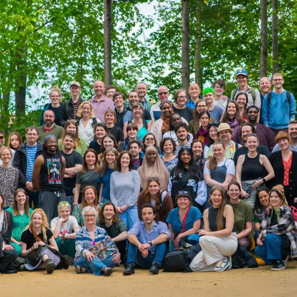 A large posed group of 100+ people facing towards the camera, with green trees behind them