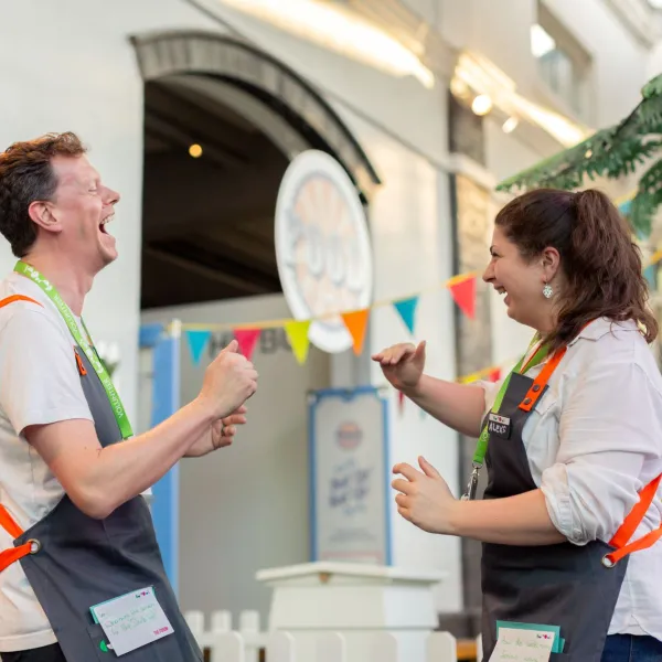 Two volunteers wearing grey aprons looking at each other and laughing