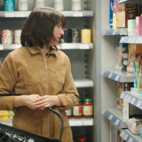 A person in a supermarket, carrying a shopping basket and looking at items.