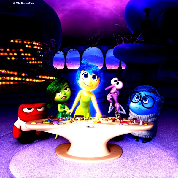 Promotion picture for the animated film Inside Out featuring the main character Ryle standing behind a table surrounded by animated figures representing her emotions 