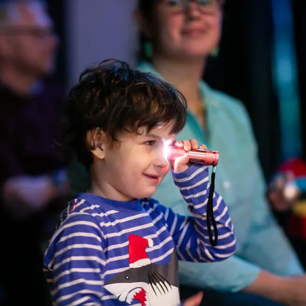 A small child is holding a torch up to it's eye, in a studio space.