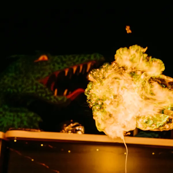 A dragon is in the background of the image with it's mouth open. To it's right in the foreground is a bright yellow flame. Taken from a demonstration from Fariytale SOS studio show at We The Curious