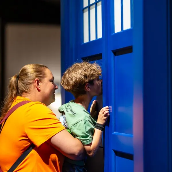 An adult is lifting up a child to peer into the TARDIS in a science centre.