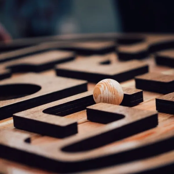 A wooden panel with a maze carved into it with a wooden ball resting on top of it.