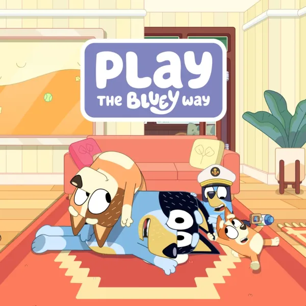 A still from the Bluey animation series. It shows a cartoon dad dog smiling being piled on top of by the rest of his family. The still carries the words 'Play the Bluey Way'