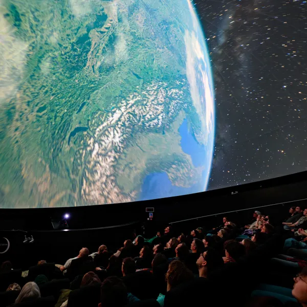 Image shows view of audience in the planetarium. On the screen is an image of Earth from orbit.